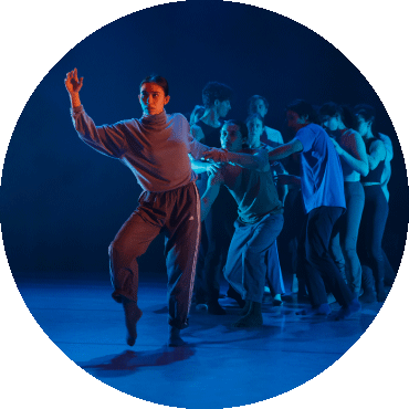 Dancer holds a stance on stage with dancers behind them