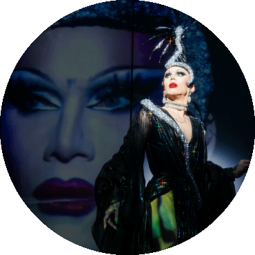 Sasha Velour poses looking to the side with an image of themselves projected behind