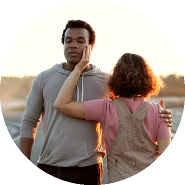 Two people face different directions with one person's back to the camera and their hand on the other's face