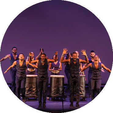 Group of dancers perform on stage against a purple background