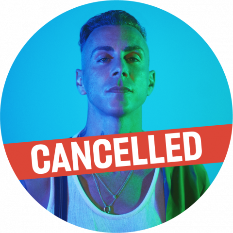 A circular bust shot of Asaf Avidan. He has light skin and short dark hair that is shaved on the sides. He looks at the camera, with half of his face in purple light and the other side is lit by green lights. He has black tattoos on his neck. He wears a white sleeveless top and black suspenders. There is a red "Cancelled" banner along the bottom.