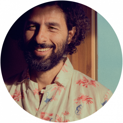 José González wears a printed shirt and smiles against a blue and brown backdrop