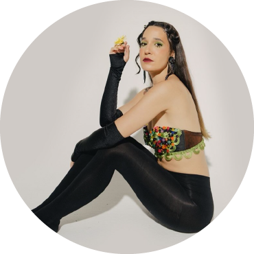 iLE poses against a white backdrop wearing a colorful top and black pants