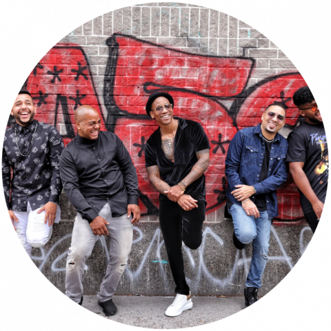 5 band members stand in a line leaning up against a graffitied wall