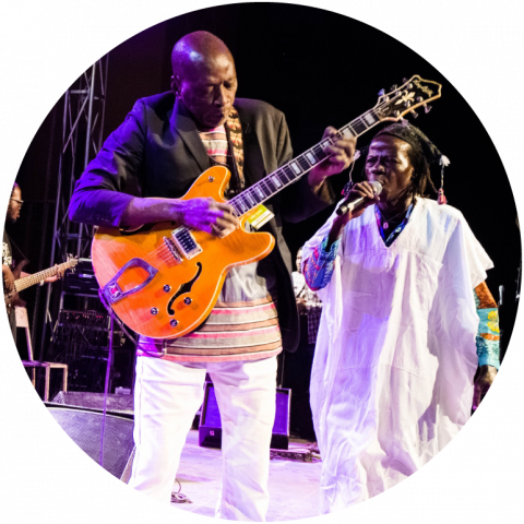 a member of the band performs live on stage with a guitar, while another member wears white and holds a mic