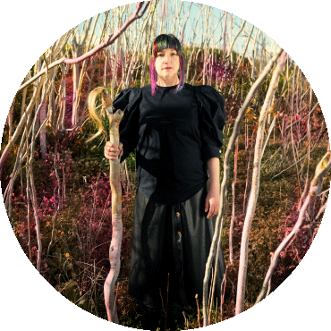 Maria Mazzotta stands among trees in a black outfit