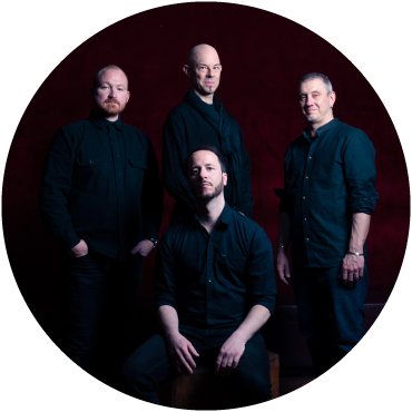 The group wears black clothing and poses against a brown backdrop