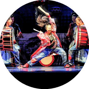 A yamato performer plays two large drums that are being held by two more yamato performers