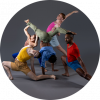 The dancers are captured together in motion wearing multicolored clothing against a gray backdrop