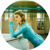 Coeur de Pirate stands in a long sleeved blue sparkly dress leaning with her left arm on a white piano. She looks down at the piano.