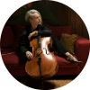 Zoë Keating poses with the cello on top of a red couch.