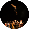 A dancer jumps in the air with a group of dancers below them
