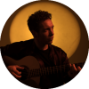 Pipo Romero holding a guitar and looking to the side 