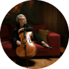 Zoë Keating poses with the cello on top of a red couch.
