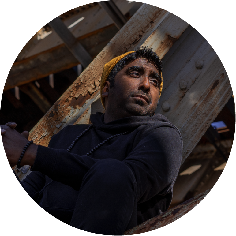 Zeshan B wearing a dark hoodie and sitting under a bridge