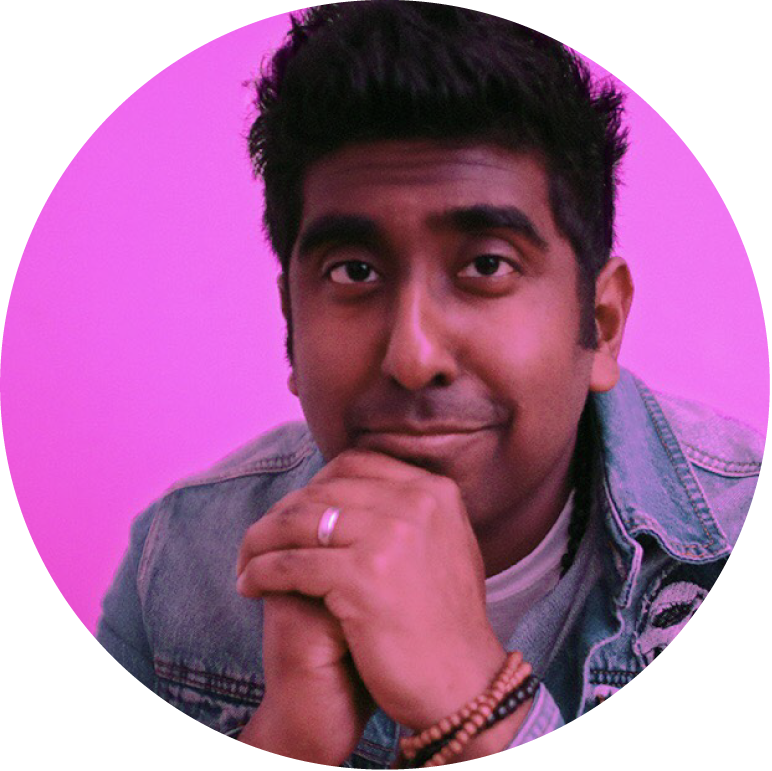 Zeshan B with a pink background looking into the camera with his hands by his face, clasped