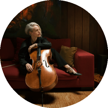 Zoë Keating poses with the cello on top of a red couch.