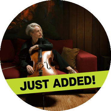 Zoë Keating poses with the cello on top of a red couch.